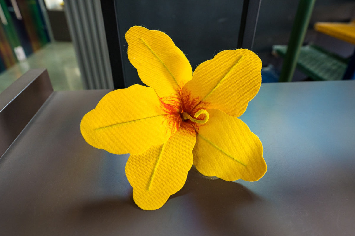 A yellow fabric flower rests on a table, its woven petals catching the light.