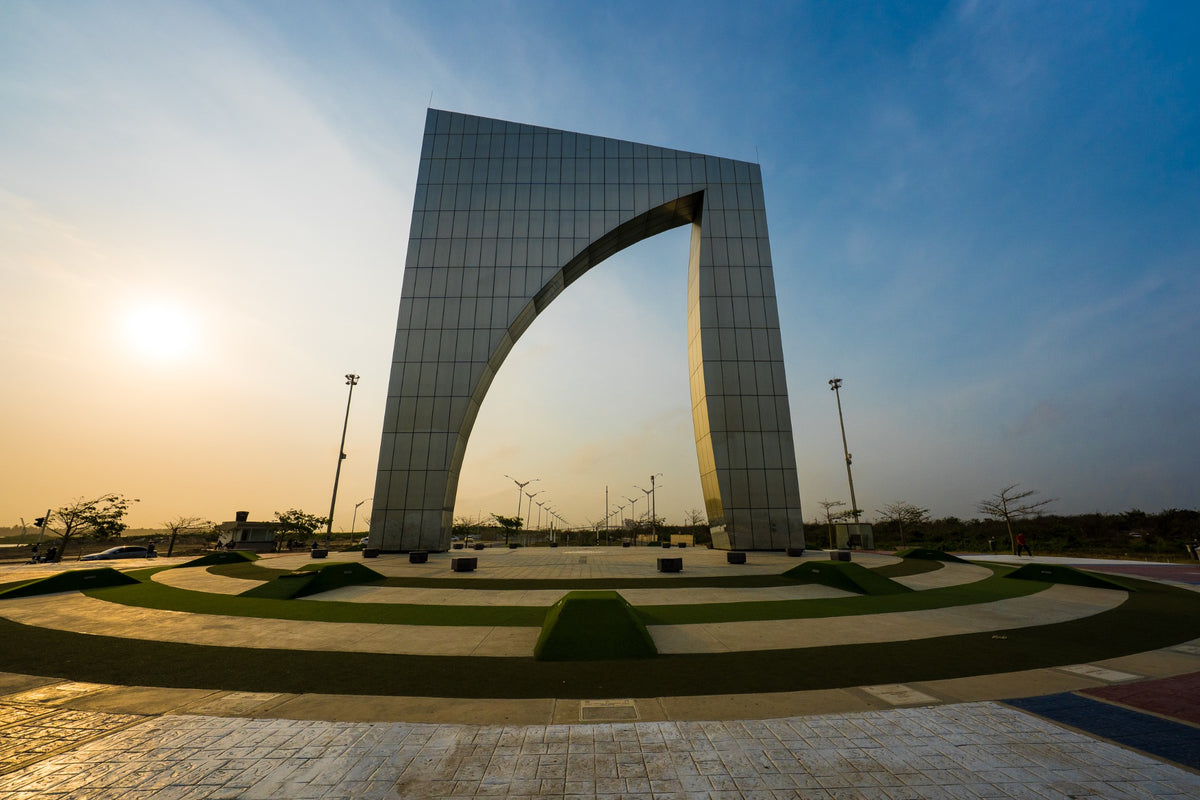 A monumental arch rises above a plaza in the warm light of the low sun.