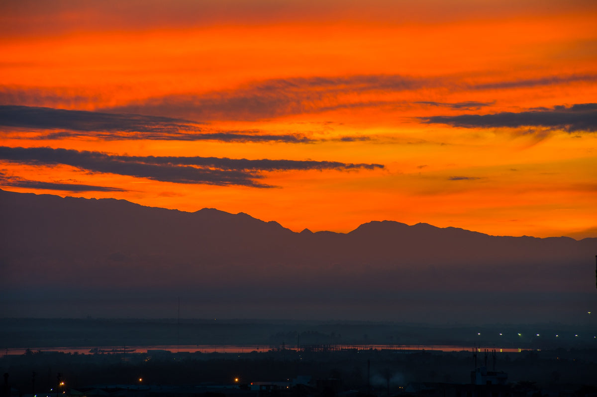 An orange sky glows above a distant mountain silhouette and dark city rooftops.