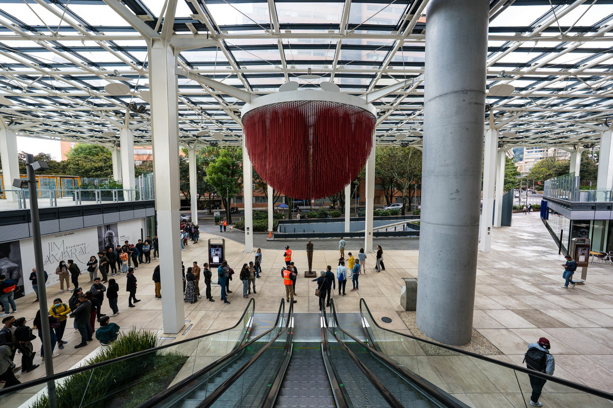 A red suspended sculpture above people and escalators in a glass-roofed atrium.