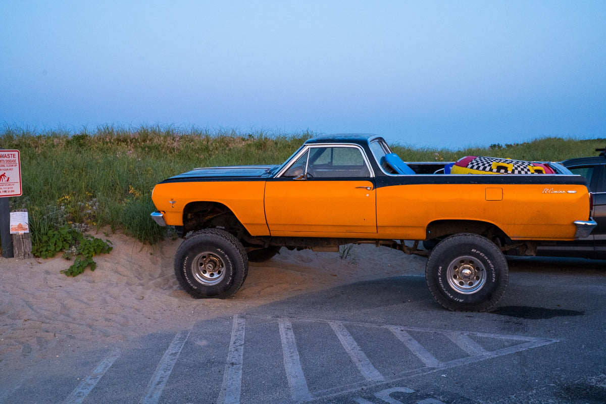 An orange El Camino stands tall at the dunes, carrying the beach day into the blue hour.