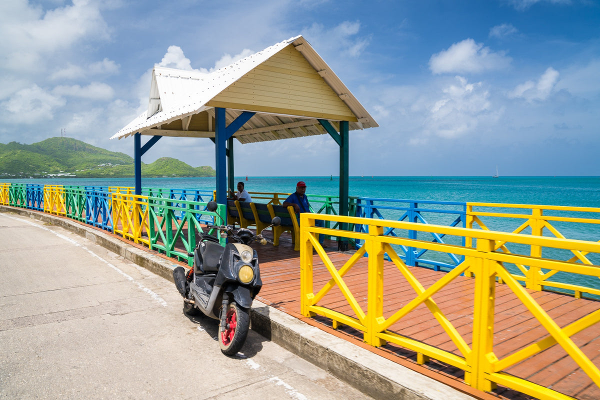 A colorful seaside shelter, two seated people and a parked motorbike.
