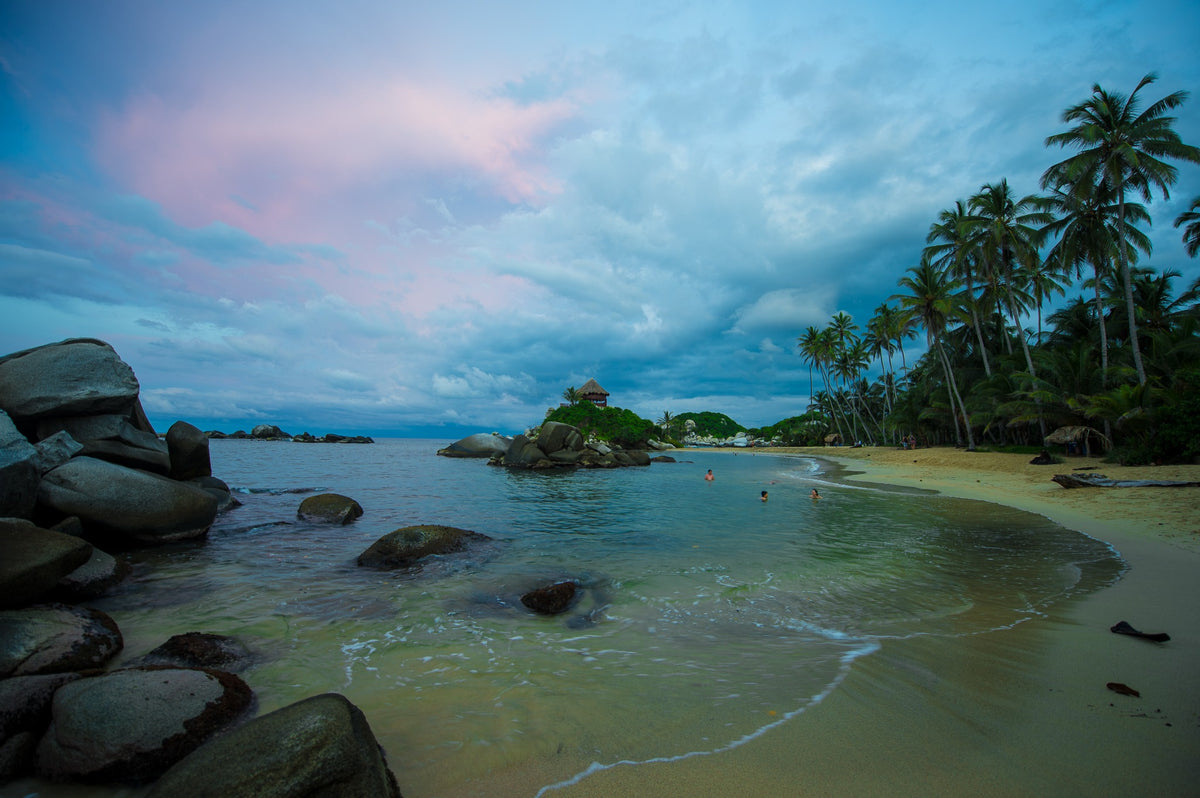 A curved beach, palms and the thatched lookout at El Cabo beneath softly colored clouds.