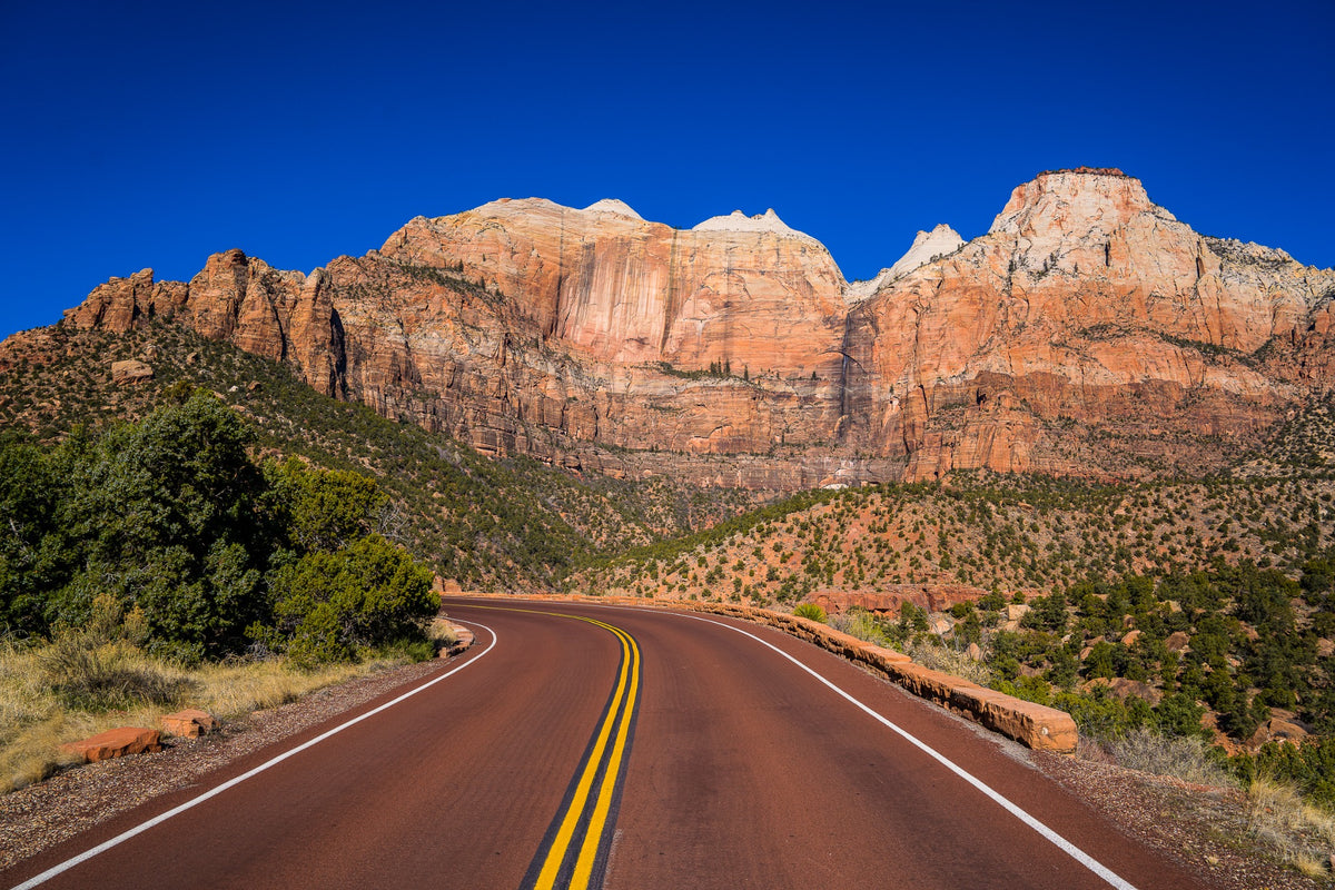A curving red road leads toward towering pale sandstone cliffs.