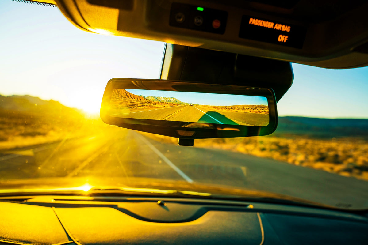 A rearview mirror reflects a desert highway in golden light.