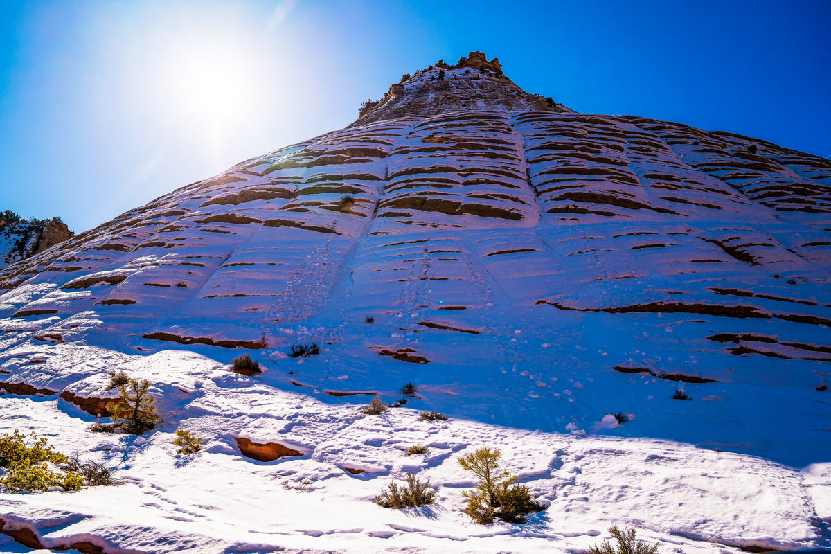 Snow traces horizontal sandstone layers beneath a brilliant blue sky.
