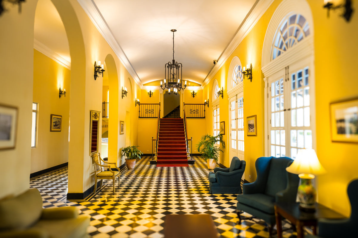 A golden yellow hallway with a checkerboard floor, arched windows and a red staircase.