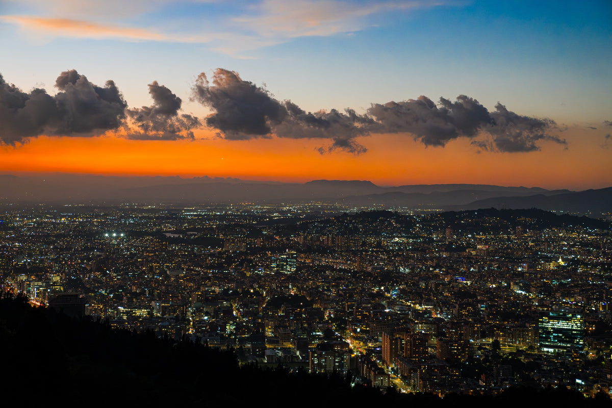 Bogotá’s evening lights beneath an orange horizon and dark clouds.