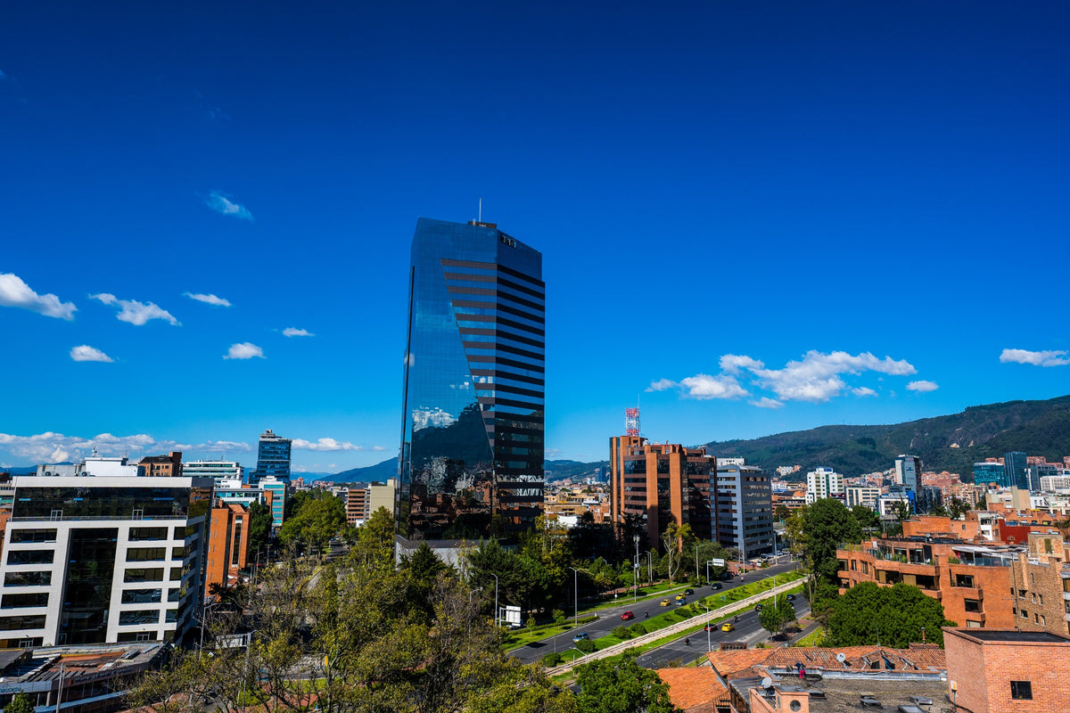 A blue glass tower rising above brick rooftops beneath Bogotá’s clear sky.