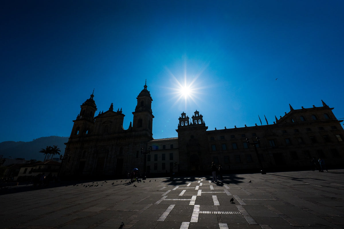Cathedral silhouettes and pigeons on a sunlit square beneath a deep blue sky.