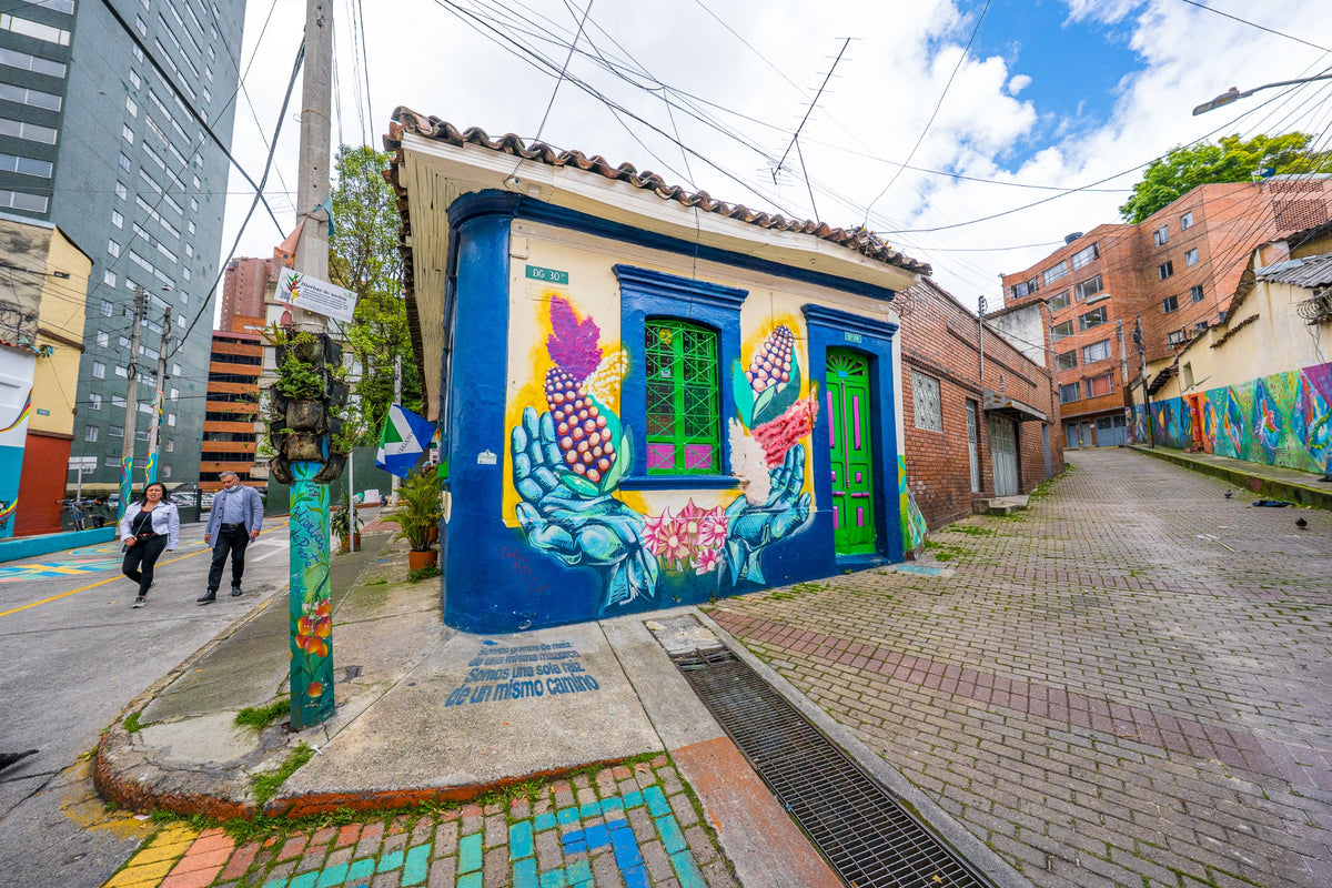 A corner house painted with bright corn and hand murals, beside a cobbled lane.