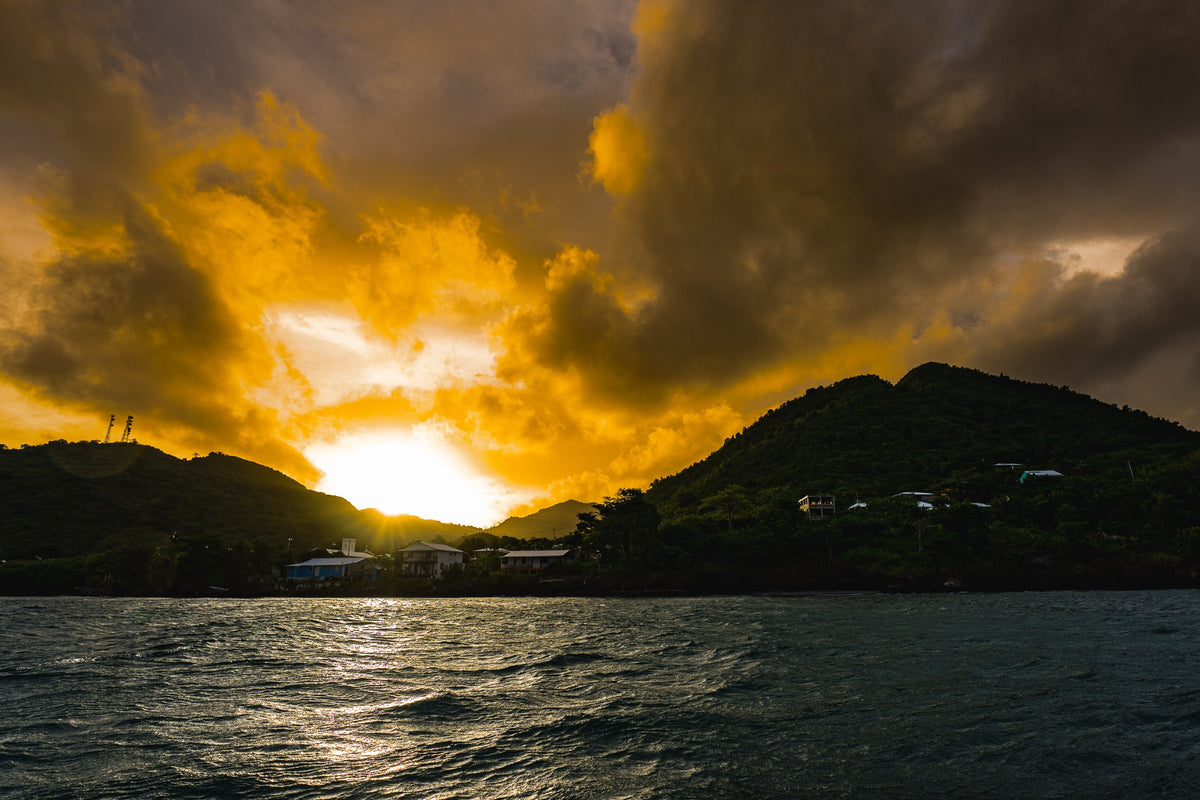 Golden sunlight breaks between island hills beneath dramatic clouds.