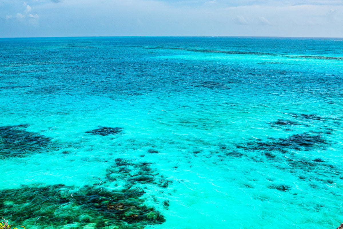 Luminous turquoise water reveals dark reef shapes beneath the surface.