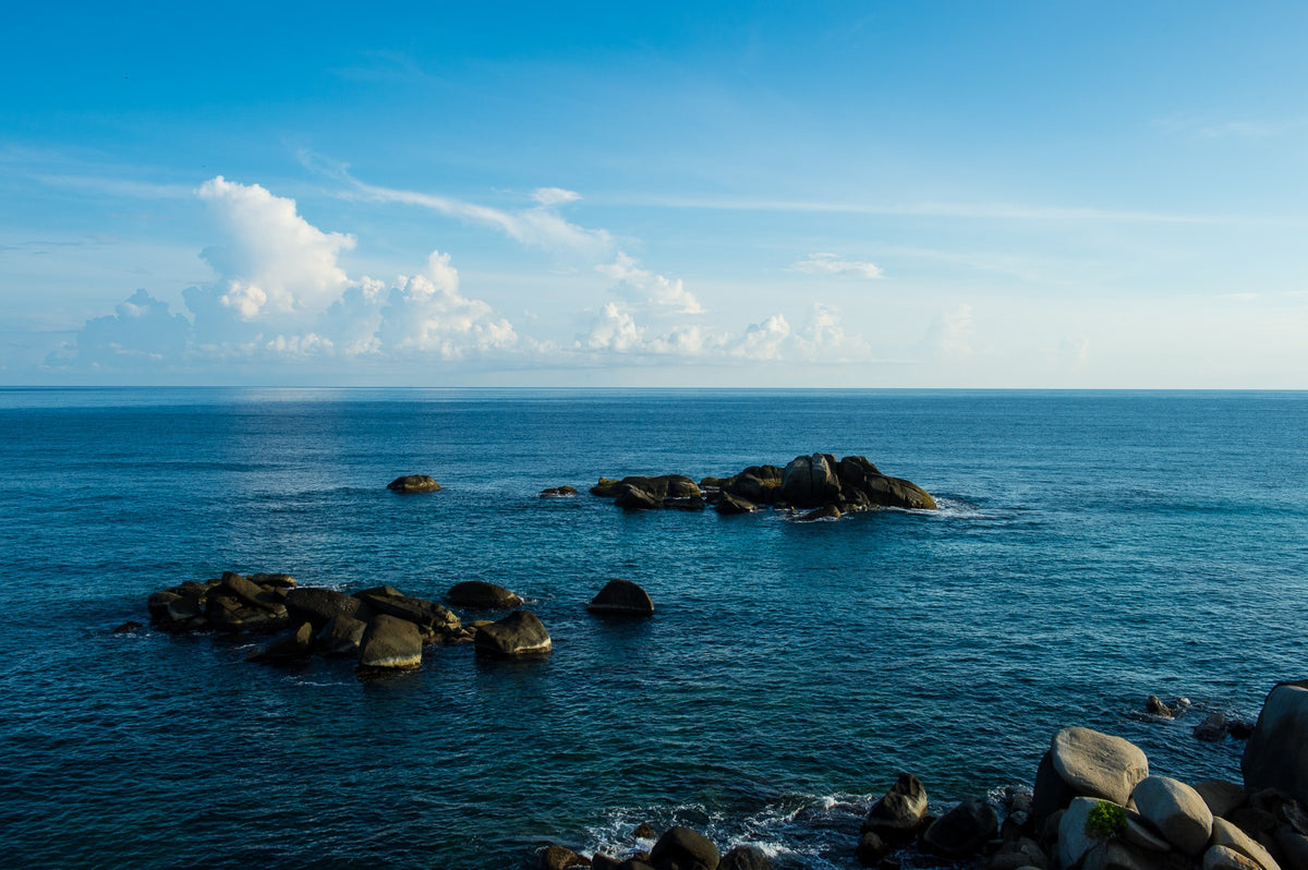 Offshore boulders punctuate a blue Caribbean horizon beneath white clouds.